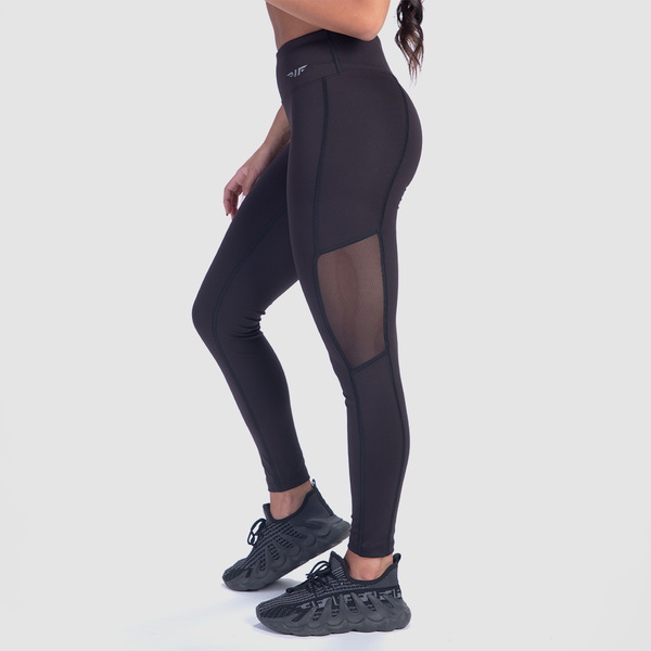 a fit woman stand at right and wearing  legging black with little mesh fabric black , plus she wearing  sneakers black 