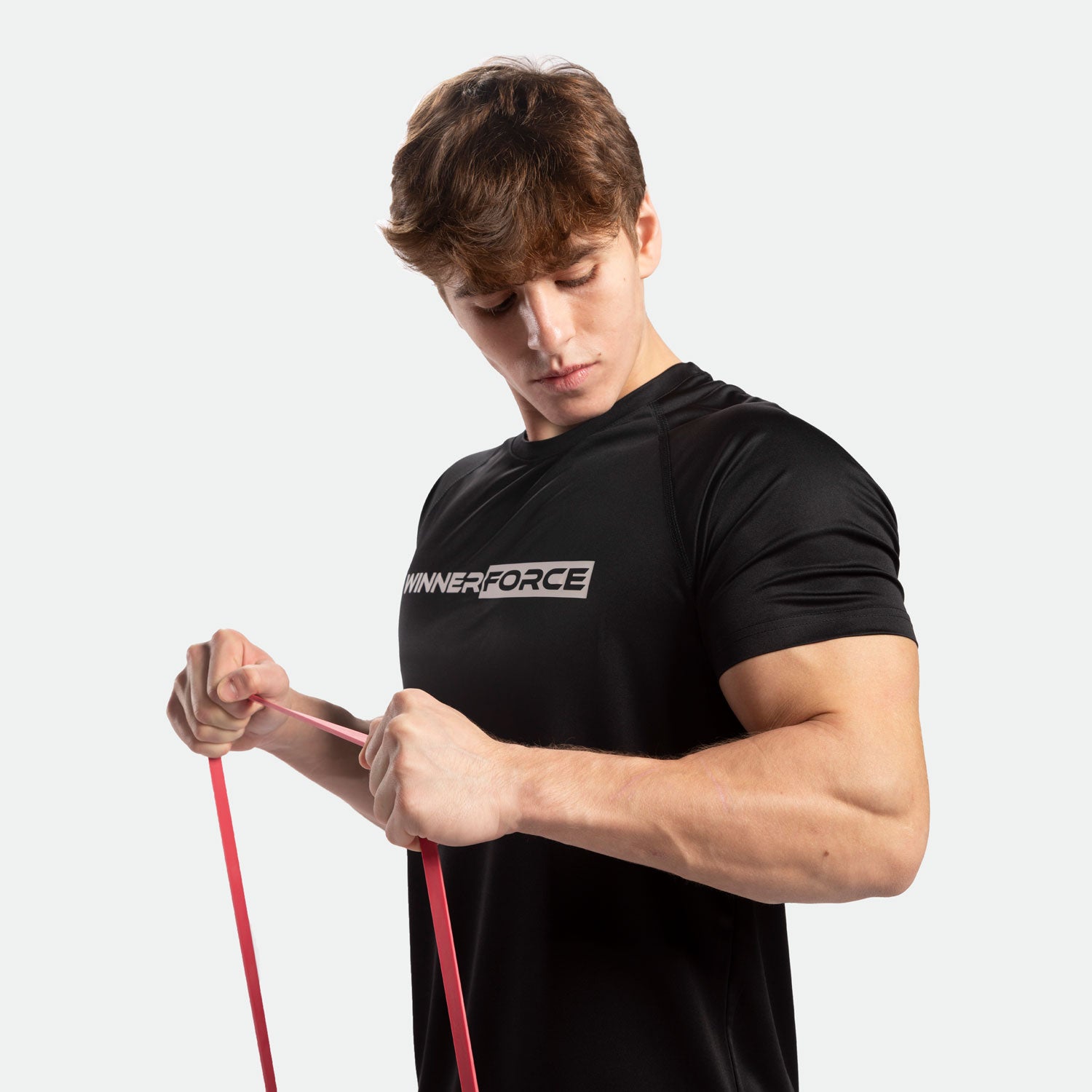 A man in a black "Winnerforce" shirt focuses intently while stretching a red resistance band. His expression conveys determination and strength.