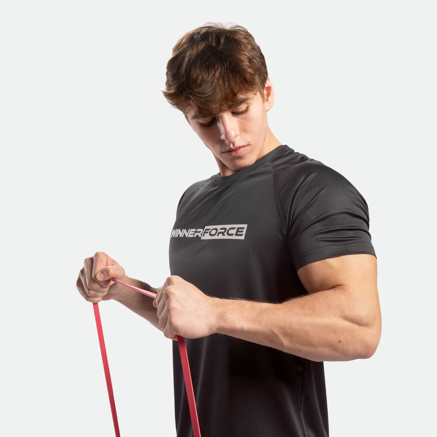 Athletic man in a black "Winnerforce" shirt pulls a red resistance band, focusing intently. 