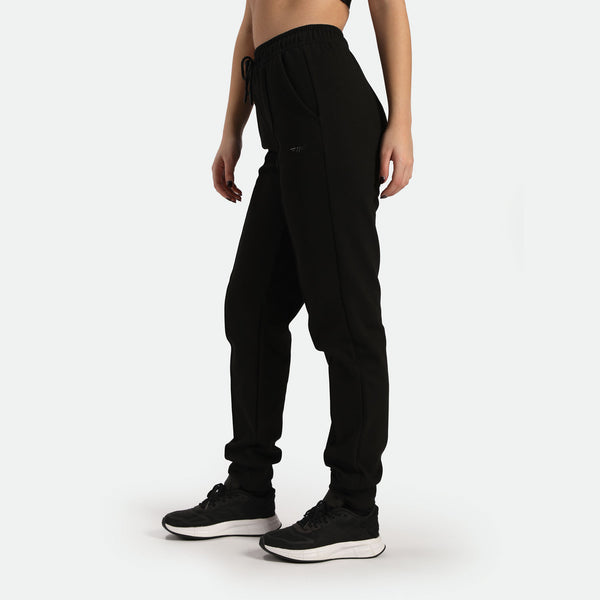 a fit woman stand at right and wearing black jogger pants with shoes ,plus the background is light grey 