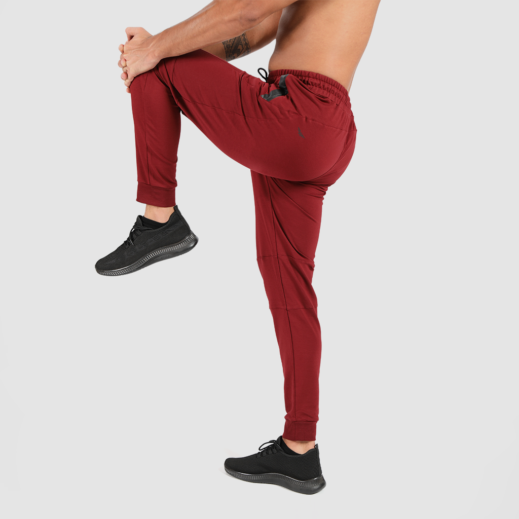 a fit man stand at right with pose and wearing pants dark red with shoes black 
