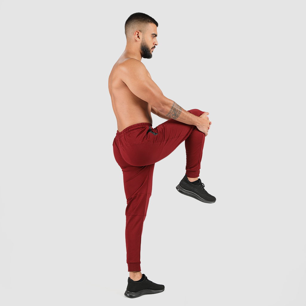 a fit man stand at right with pose and he wearing pants dark red with shoes black 