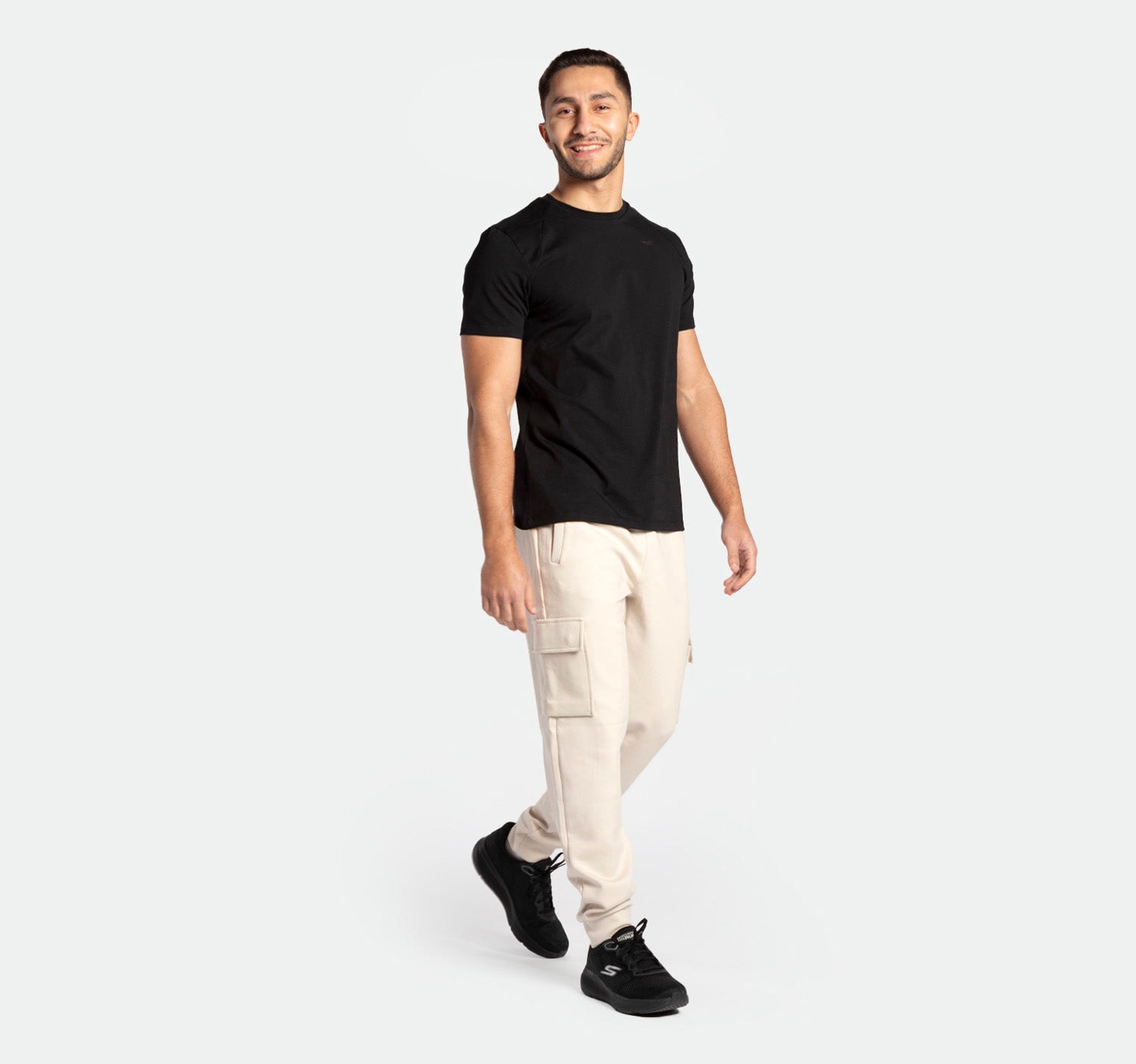 close up view  for fit man ,he stand with pose and smile ,he wearing t-shirt black  with  jogger pants light beige  ,plus the shoes black  