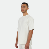 a fit man stand at right and wearing matching set off white ,t-shirt and short 