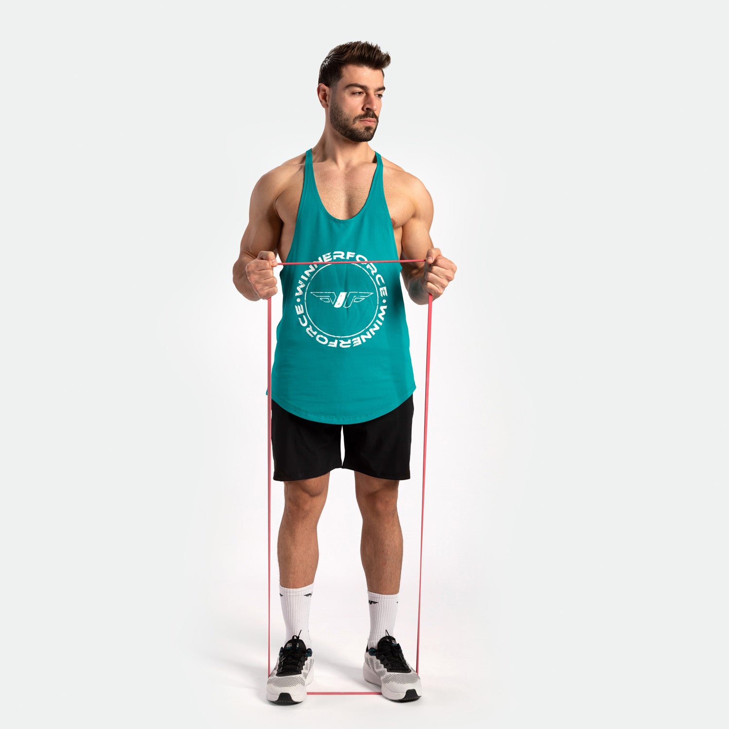 A man in a title blue  tank top and black shorts exercises with a red resistance band. He stands confidently, wearing white sneakers, on a plain background.