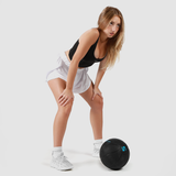 Person in athletic wear leaning forward with hands on knees, appearing to rest after exercise. Wearing a black tank top, white shorts, and white sneakers, with a black medicine ball labeled '5' on the ground in front