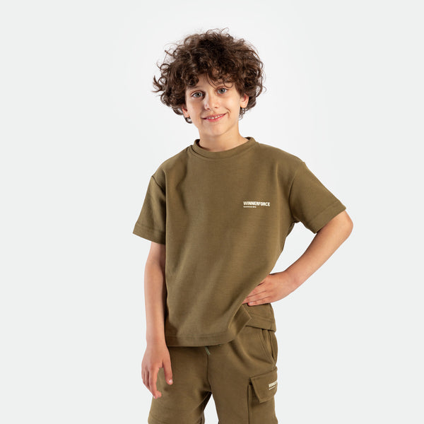a young boy look at the camera and smile ,he wearing matching set olive drape , t-shirt with logo and short with tow pocket 
