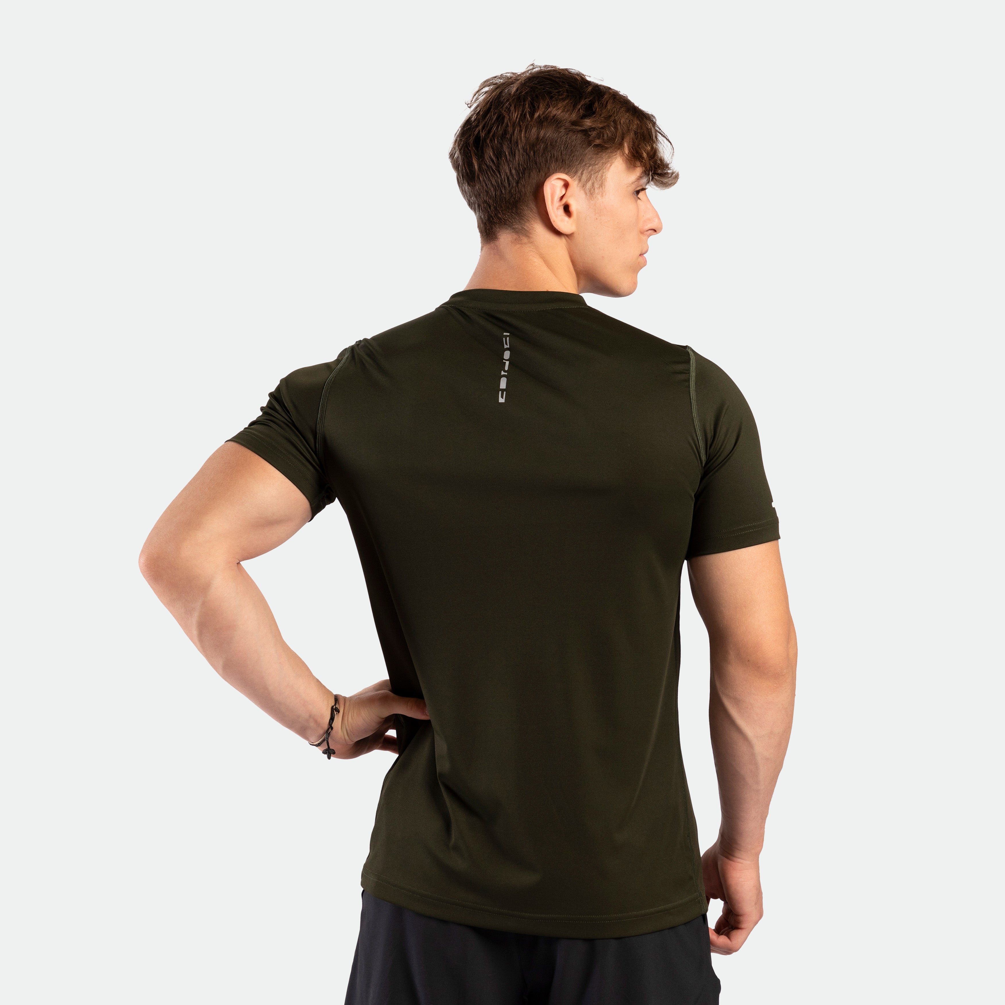 Back view of a man posing and wearing a performance fit t-shirt in the color dark olive. He is also wearing the tri short.