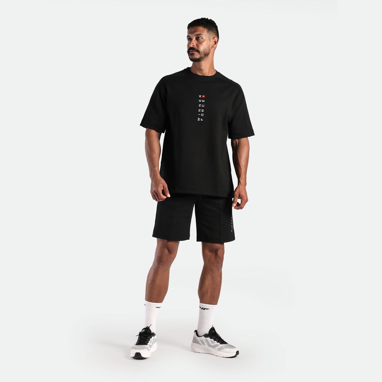a fit man wearing matching set black ,t-shirt with logo and short ,plus the socks white and shoes 