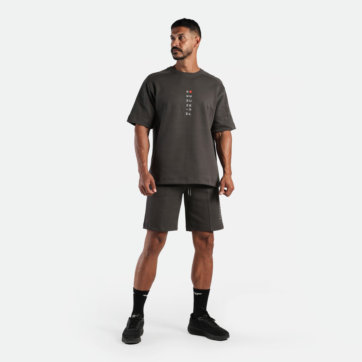 a fit man wearing matching set iron dark grey , t-shirt with logo and short ,plus the socks and shoes black 