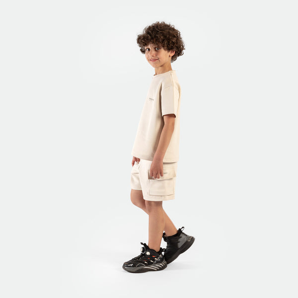 a fit boy stand at right and wearing matching set light beige ,t-shirt with short ,plus the shoes 