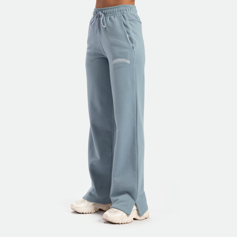 Side view of a person wearing light blue wide-leg pants with an elastic waistband and drawstring, paired with chunky white sneakers. The pants have a relaxed fit and a soft, flowy appearance