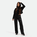 Person posing in a black hoodie and black pants, standing against a plain white background.