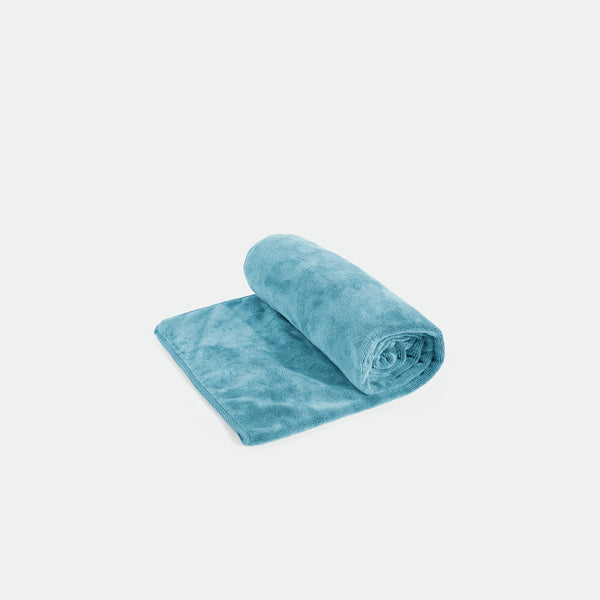 A blue bath mat is partially rolled on a light gray background, showing its soft texture and plush design. The scene conveys comfort and coziness.