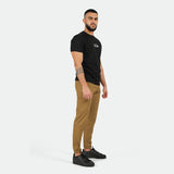 a fit man stand at right and wearing t-shirt black with logo and pants Breen brown ,plus shoes black 
