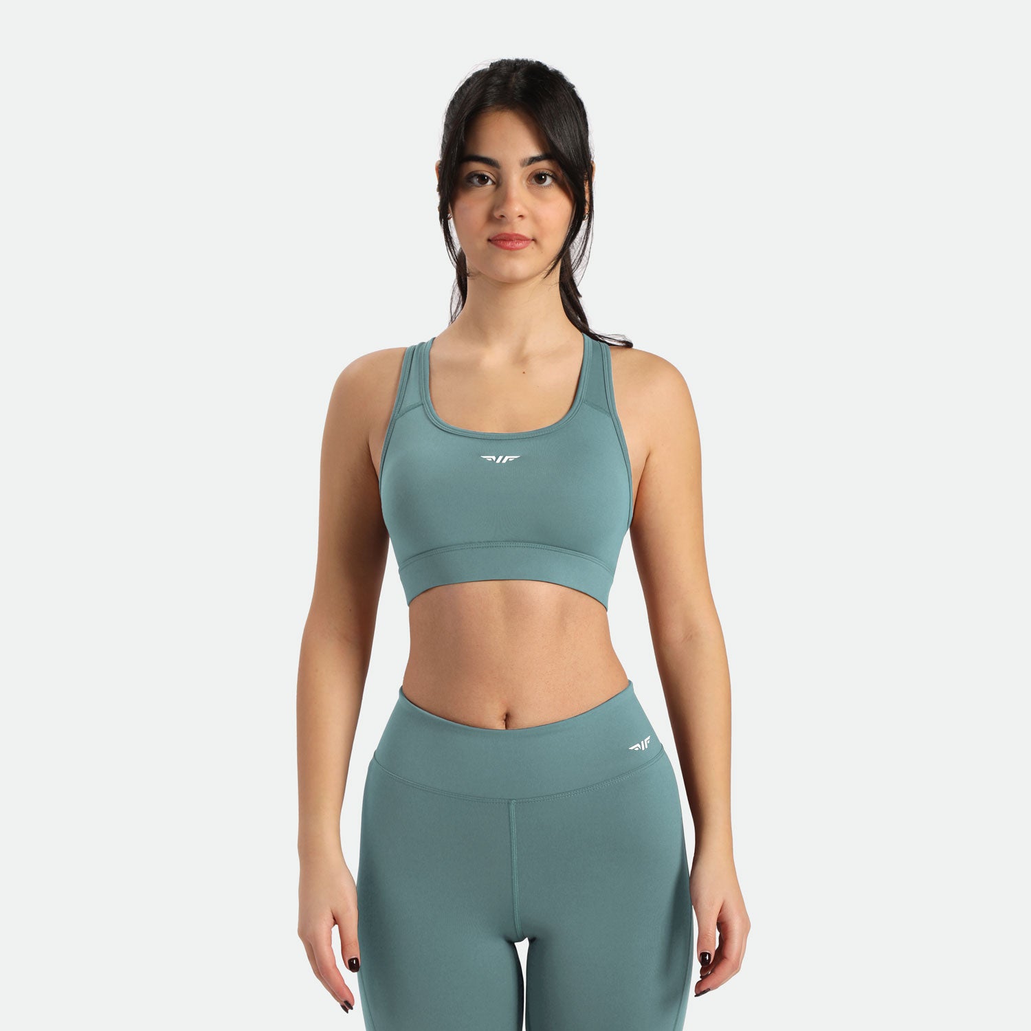 A fit young woman with dark hair in a ponytail wears a teal blue sports bra and matching leggings ,its is have same logo it includes winnerforce logo with different directions 