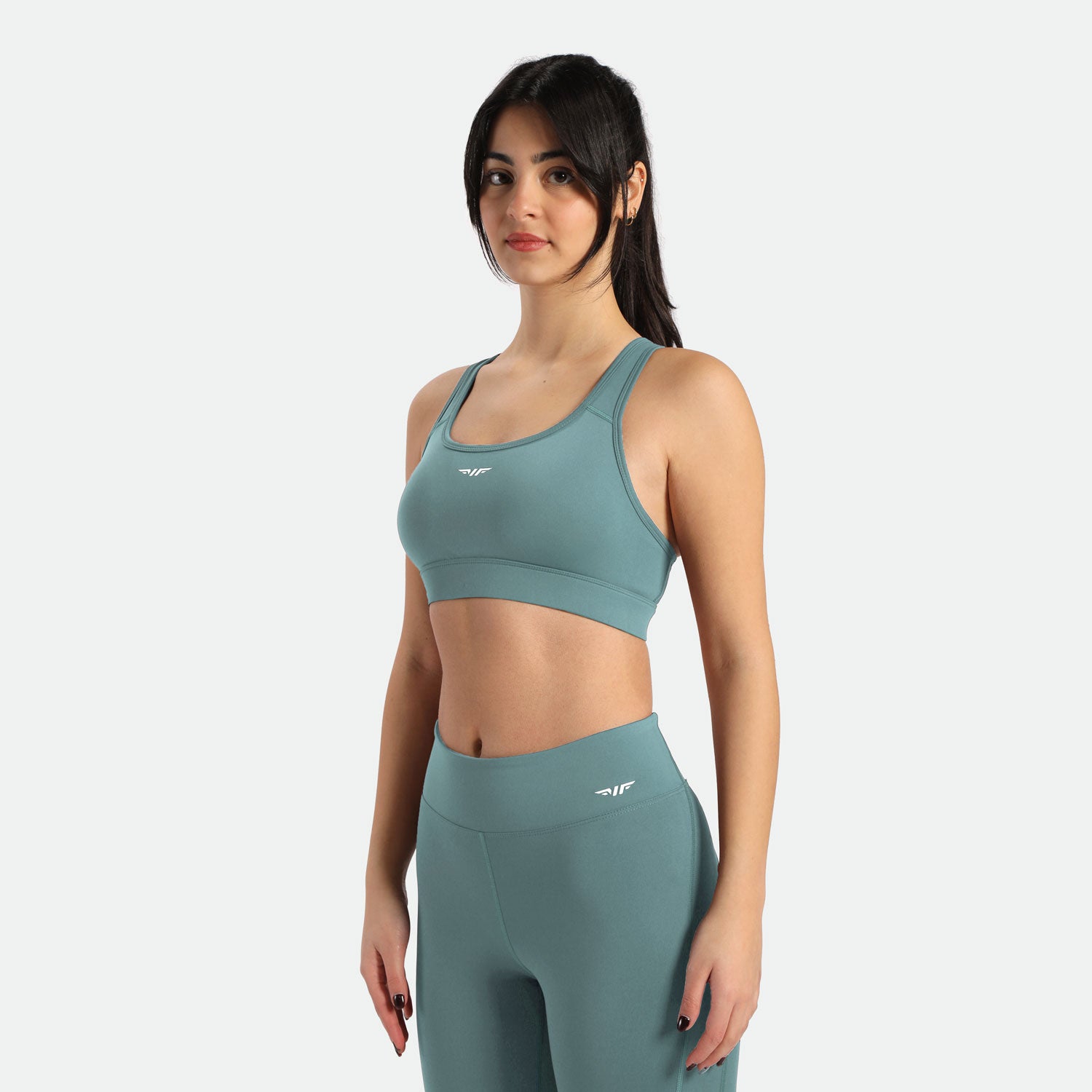 Young slim woman with dark hair tied in a ponytail wearing a sports bra and teal leggings, it includes winnerforce logo with different directions 