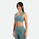 Young slim woman with dark hair tied in a ponytail wearing a sports bra and teal leggings, it includes winnerforce logo with different directions 