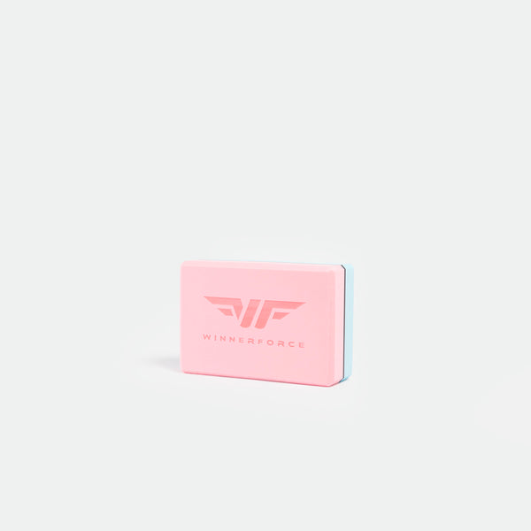 A pink, rectangular yoga block with a blue edge, featuring the logo and text "WinnerForce" in the center. The background is plain white, conveying simplicity.