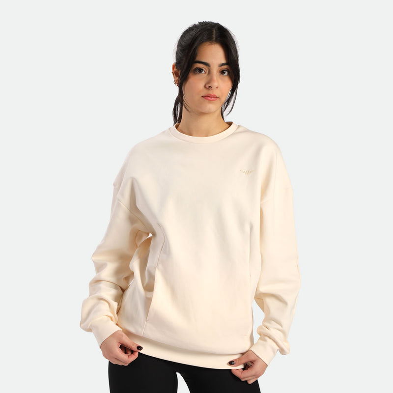 Person wearing a light beige sweatshirt with a relaxed fit, posing against a plain white background.