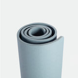 A neatly rolled, light blue yoga mat stands vertically against a plain, light gray background