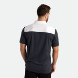 A man with short brown hair stands facing away, wearing a black and white short-sleeve polo shirt. The background is plain white, highlighting the clothing.