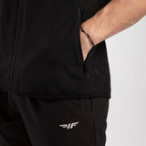 A person in black sportswear with a hand in the jacket pocket. The outfit features a white logo on the pants, conveying a sporty and casual tone.