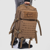  a fit man wearing tan tactical backpack with a rectangular shape, two main compartments, laser-cut MOLLE panels, side buckles, and a sturdy top handle, displayed against a plain white background.