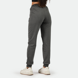 a back view for fit woman wearing dark grey  jogger pants with shoes white ,plus the background is light grey 