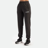 a fit woman wearing jogger pants grey with logo white and she wearing black shoes athletic ,plus the background is light grey 