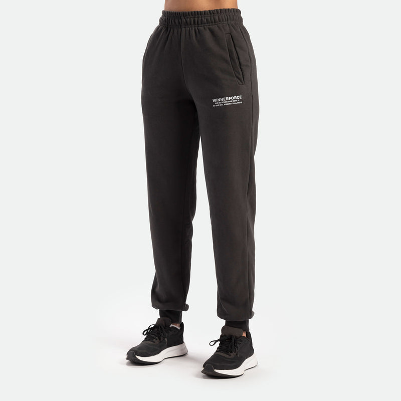 a fit woman wearing jogger pants grey with logo white and she wearing black shoes athletic ,plus the background is light grey 