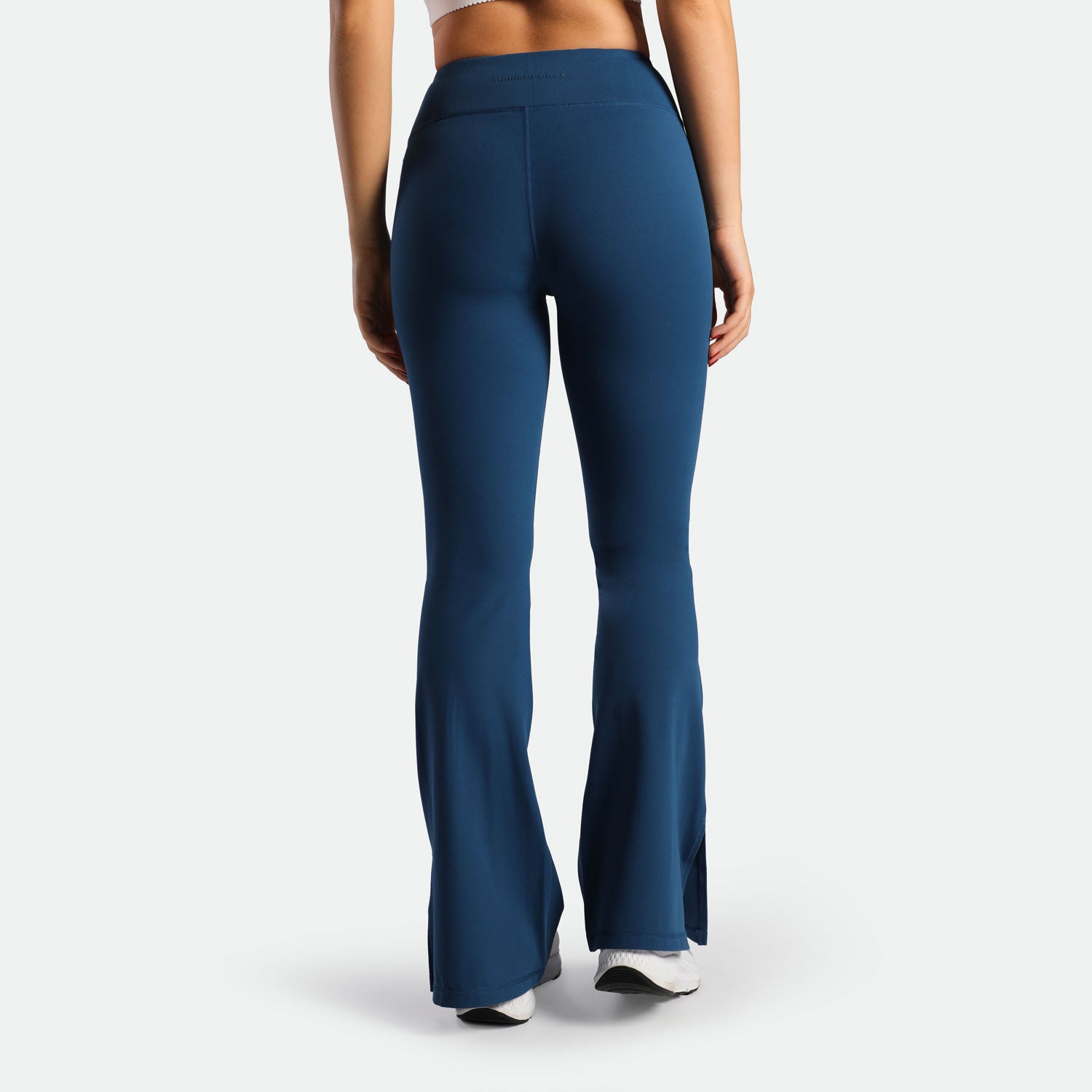 a back view for fit woman wearing flared legging Poseidon blue with shoes white 
