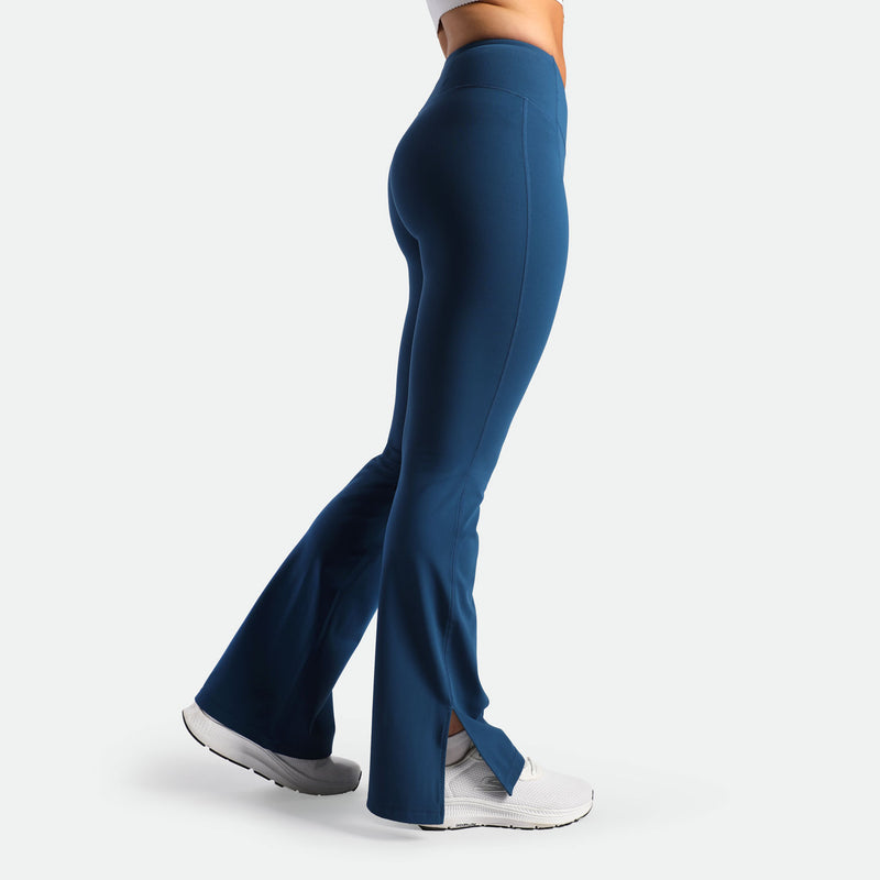 a fit woman stand at right and wearing flared legging Poseidon blue with shoes white 