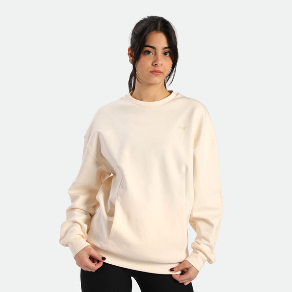 Person wearing a light beige sweatshirt with a relaxed fit, posing against a plain white background.