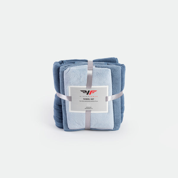 A neatly stacked towel set in shades of blue, tied with a silver ribbon and displaying a label. The image conveys softness and elegance.