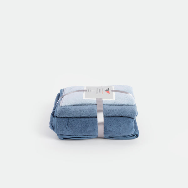 A neatly folded light blue blanket, tied with a gray ribbon, sits on a white background. A product label is visible, conveying a sense of softness and comfort.
