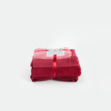 A stack of soft towels in varying shades of red, bundled together with a glossy red ribbon. A label rests on top, set against a white background.