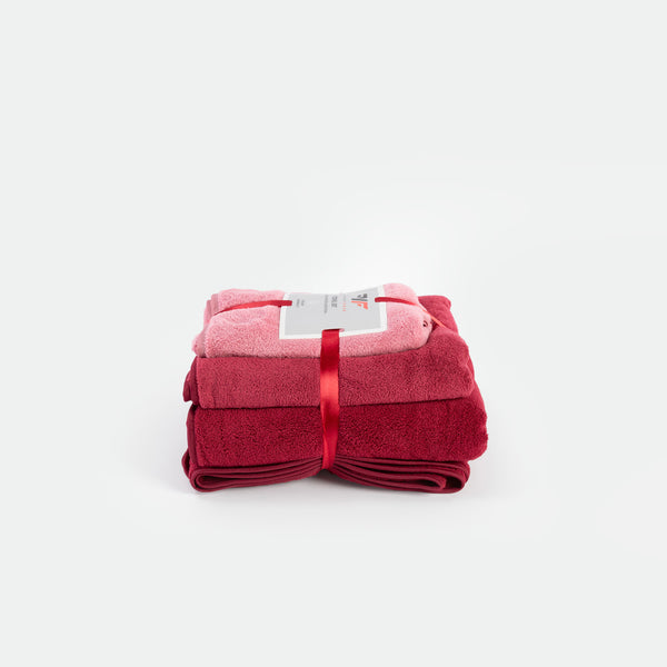A stack of soft towels in varying shades of red, bundled together with a glossy red ribbon. A label rests on top, set against a white background.