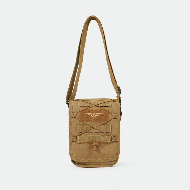 Tan crossbody bag with adjustable strap, front pocket, elastic bungee cord, and a stitched emblem featuring a stylized wing logo. The bag has a structured, utilitarian design and is displayed against a plain white background.