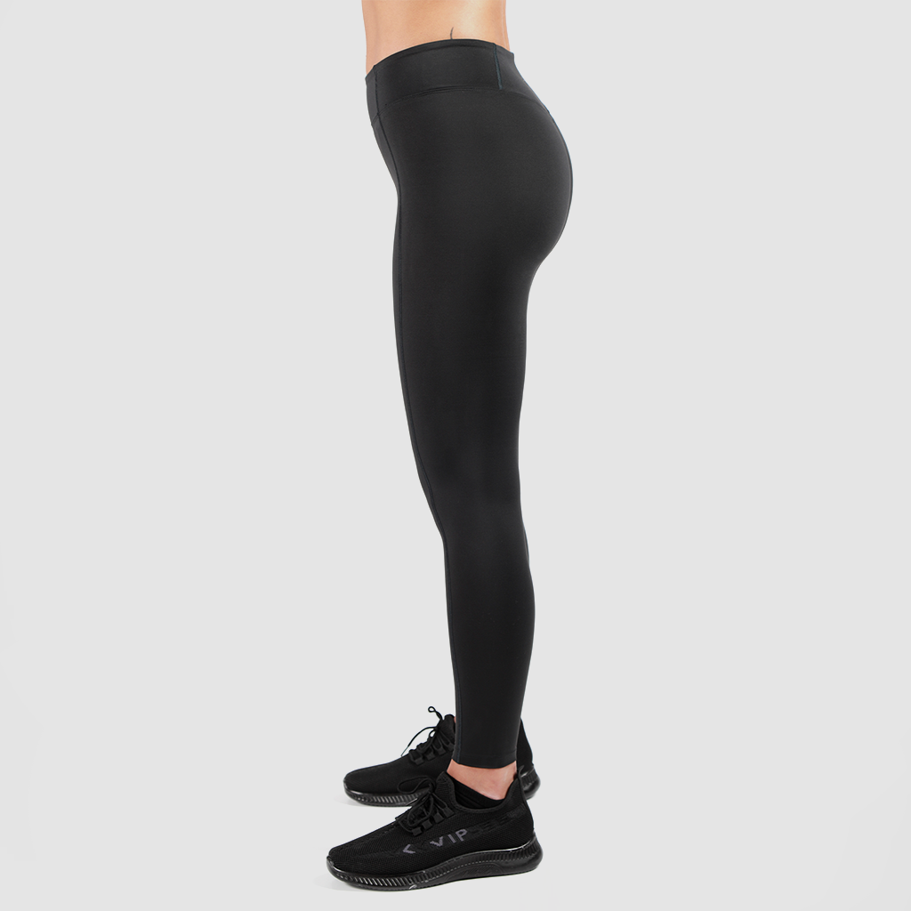 a fit woman stand at right and wearing legging black  with shoes black ,plus the background is light grey 
