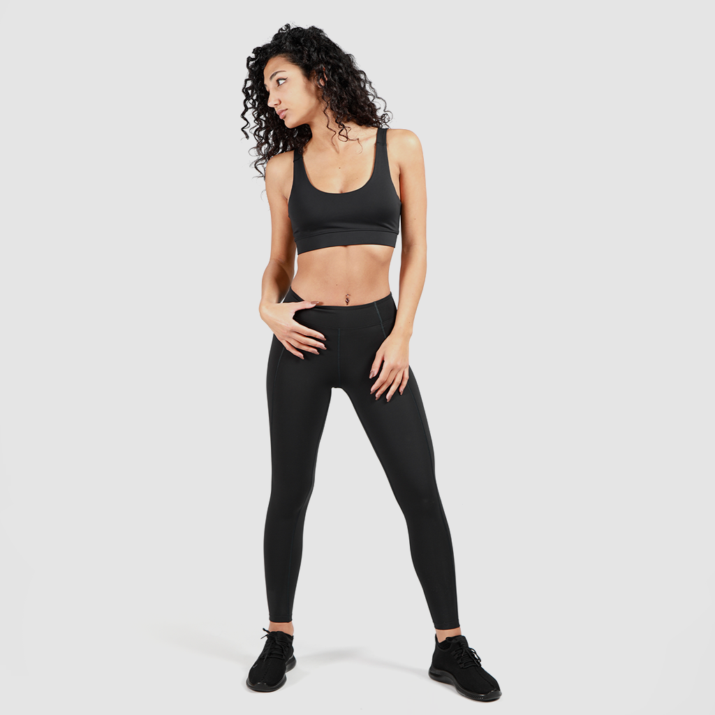 a fit woman stand with pose and wearing matching bra and legging with shoes same color is black ,plus the background is light grey 