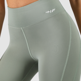 a fit woman wearing  legging olive with logo white ,plus the background is light grey 