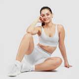 a woman wearing a matching bra and legging  gray ,she sitting on the ground and  look at the camera ,plus smiling ,the background is  light grey