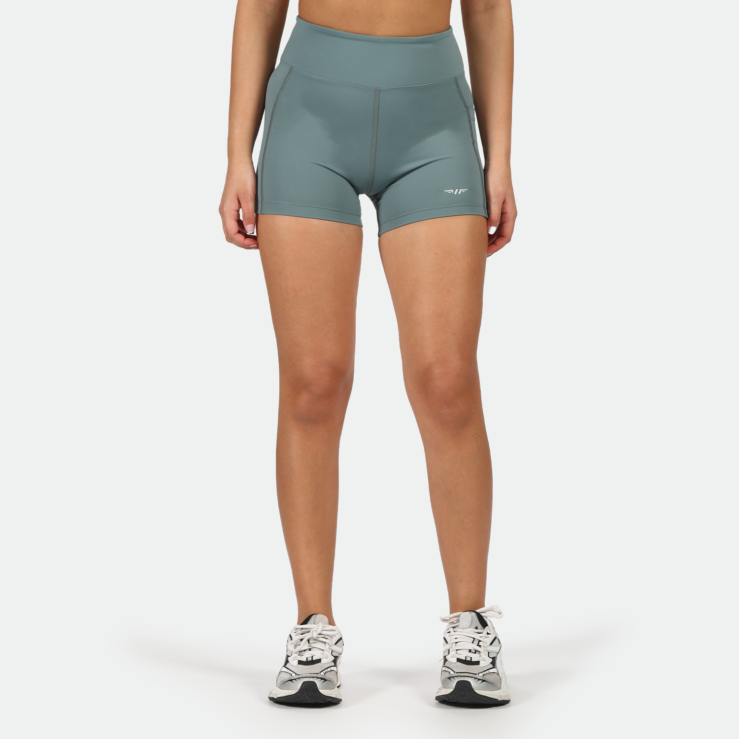 a fit woman wearing goblin blue short  with shoes ,plus the background is light grey 
