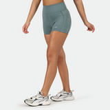 a fit woman stand at right and wearing  short goblin blue with shoes ,plus the background is light grey  