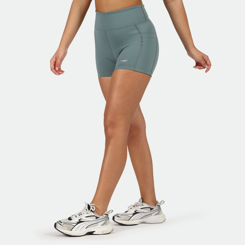 a fit woman stand at right and wearing  short goblin blue with shoes ,plus the background is light grey  