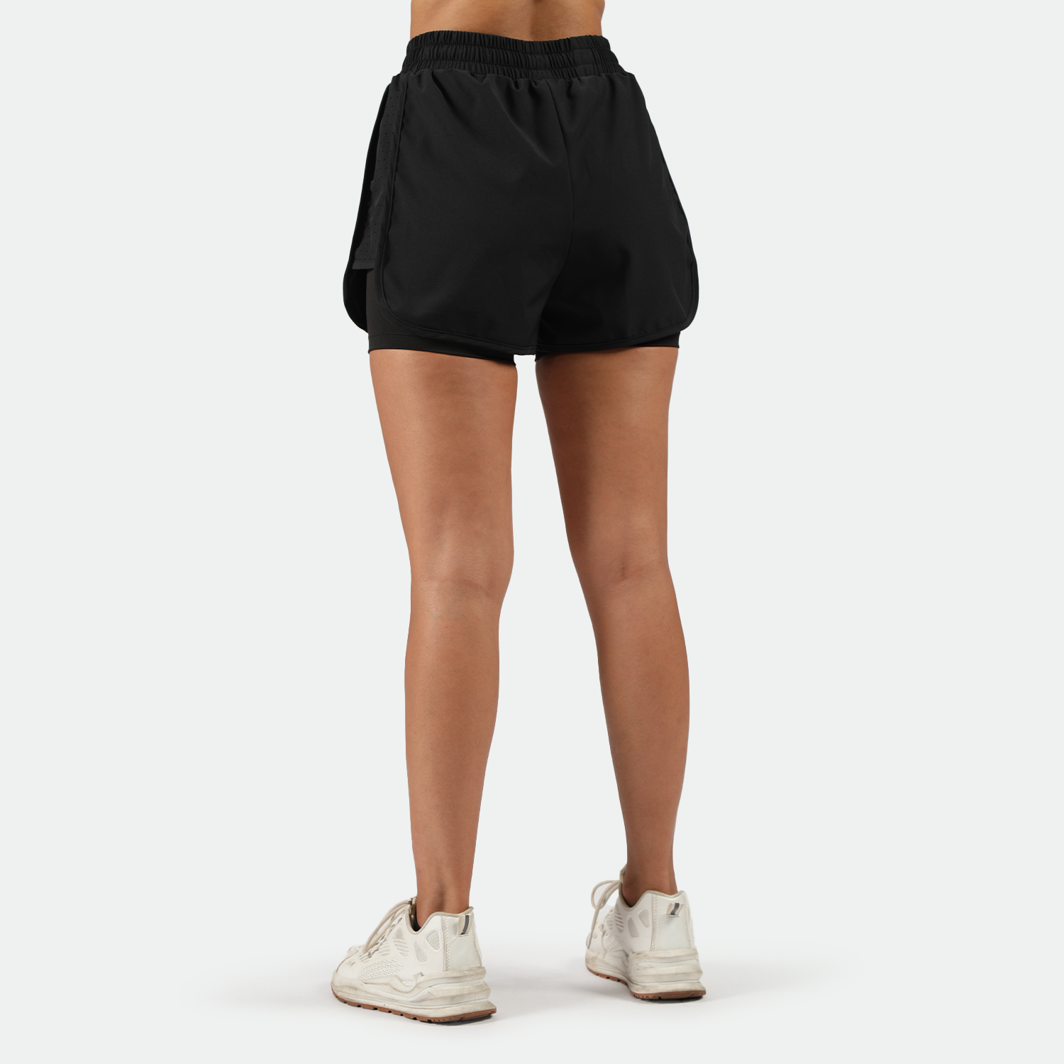 a back view for fit woman wearing black short 2 in 1,  and she wearing plus the background is light grey 