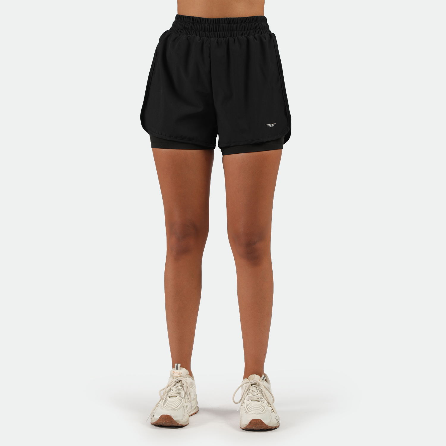 a fit woman wearing black short 2 in 1 with shoes white ,plus the background is light grey 