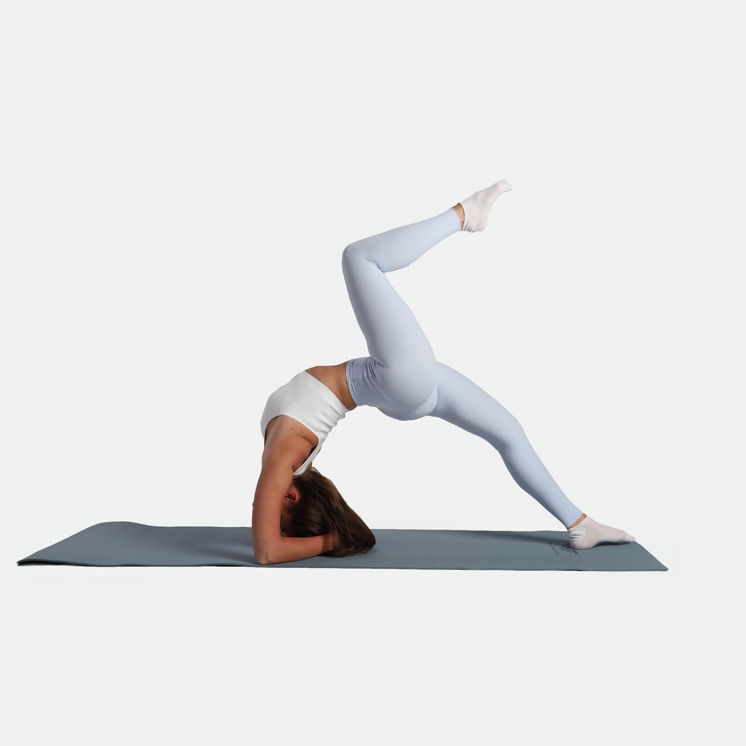 A person in a white top and leggings balances in a yoga pose on a mat, head down, one leg bent upward, conveying strength and focus.