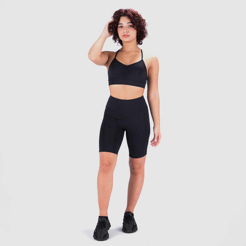  A person wearing a black sports bra and high waisted leggings stands confidently against a plain white background